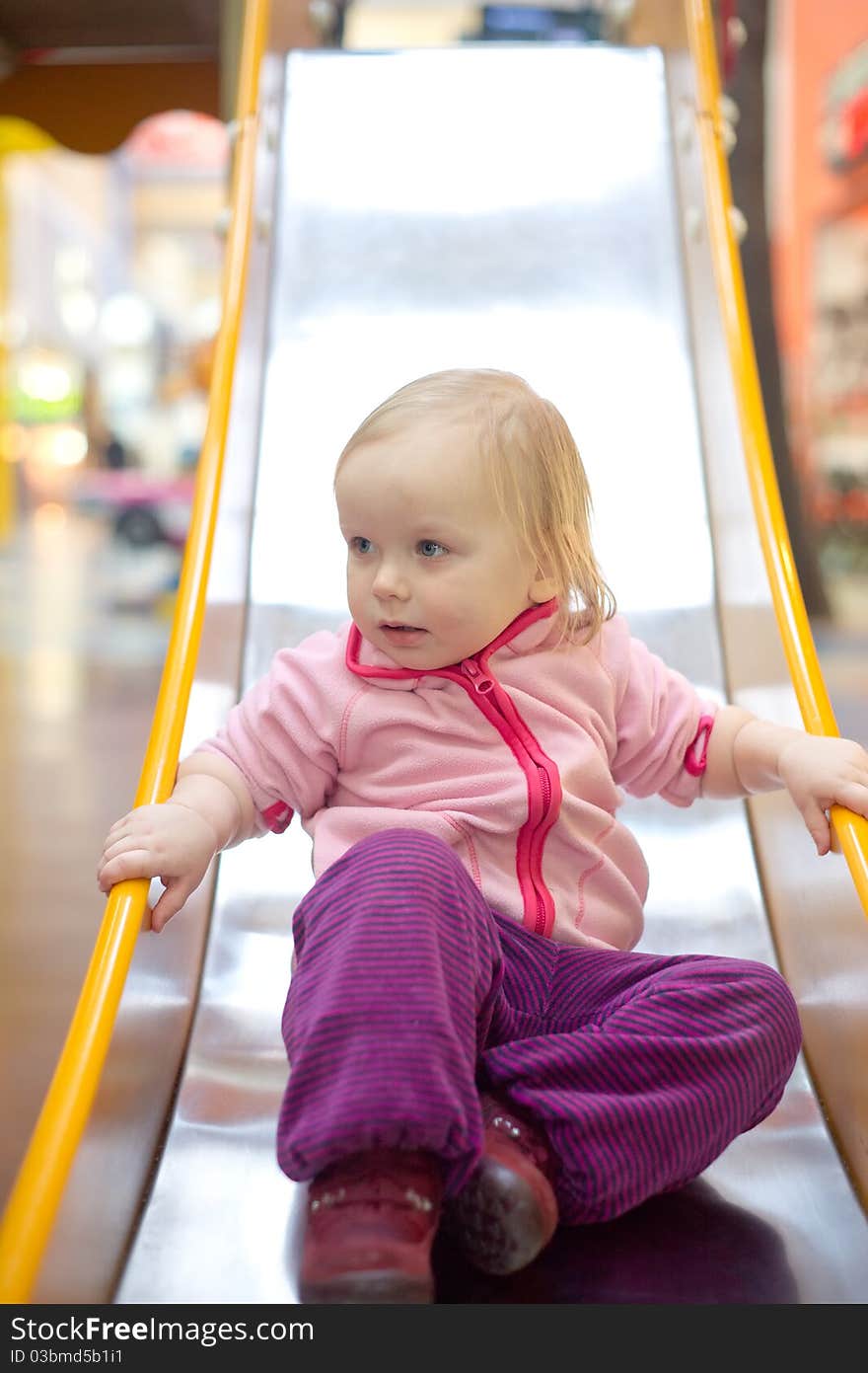 Young adorable baby sliding down baby slide on playground in mall. Sitting on the end of slide