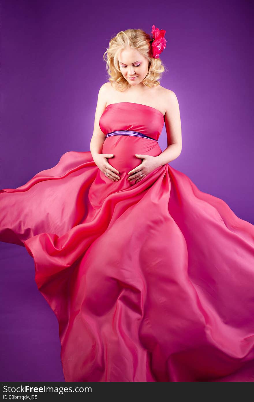 A young pregnant woman in a pink dress on the purple background. A young pregnant woman in a pink dress on the purple background