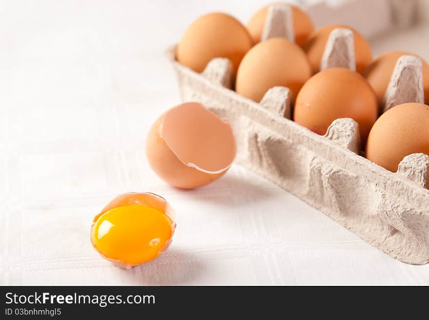 Broken brown egg beside a carton of ten eggs