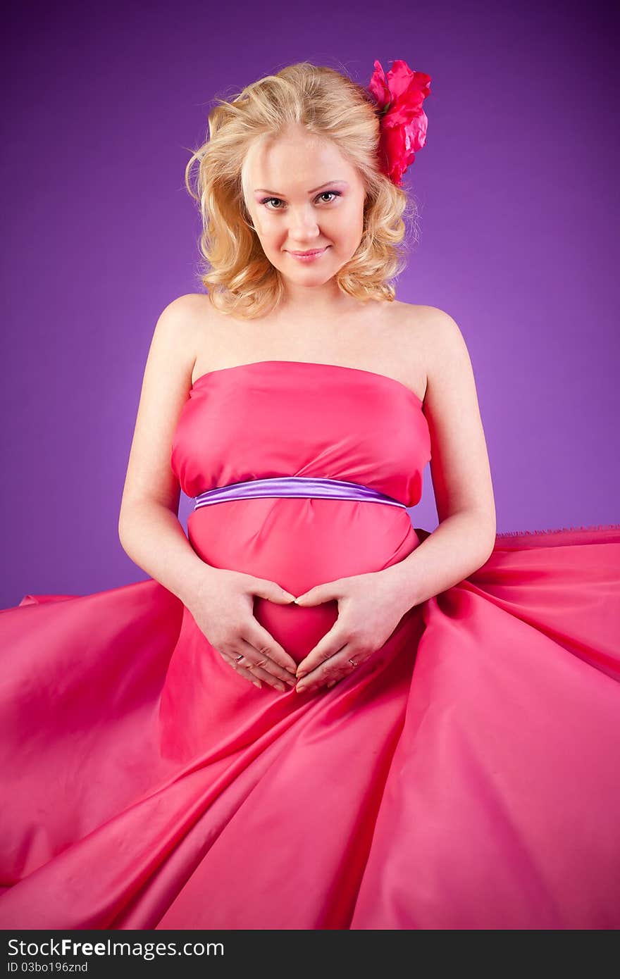 A young pregnant woman in a pink dress on the purple background. A young pregnant woman in a pink dress on the purple background