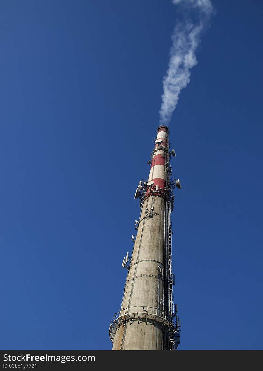 A tall chimney with smoke visible against the blue sky