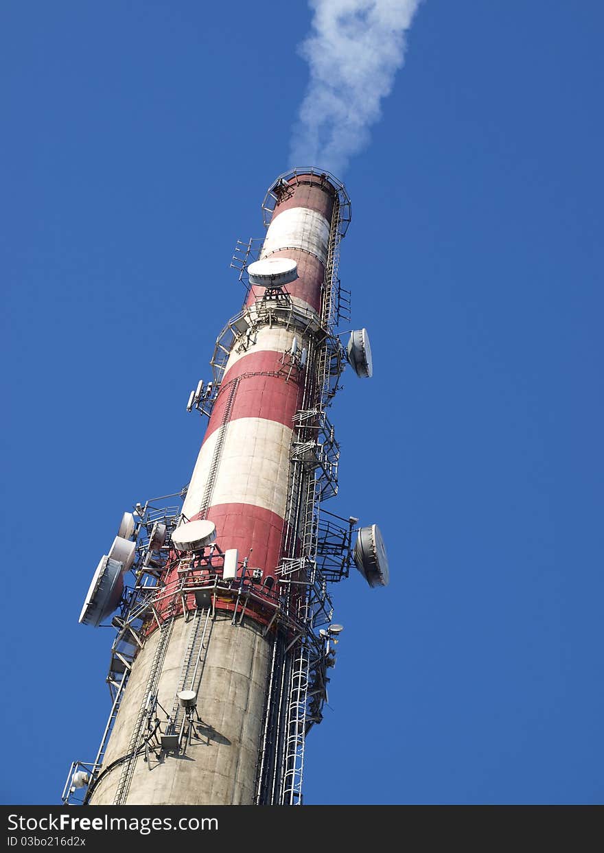 A tall chimney with smoke visible against the blue sky