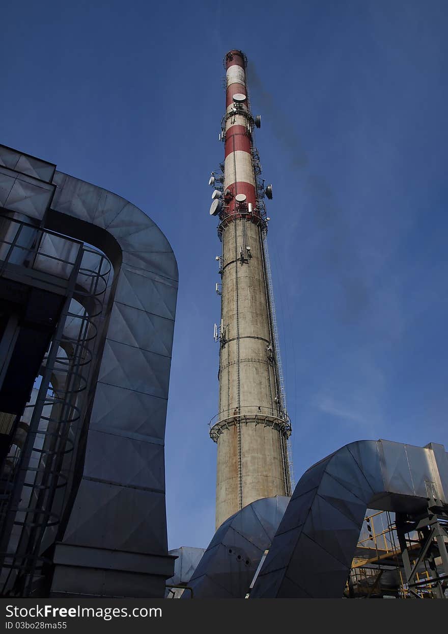 A tall chimney with smoke visible against the blue sky