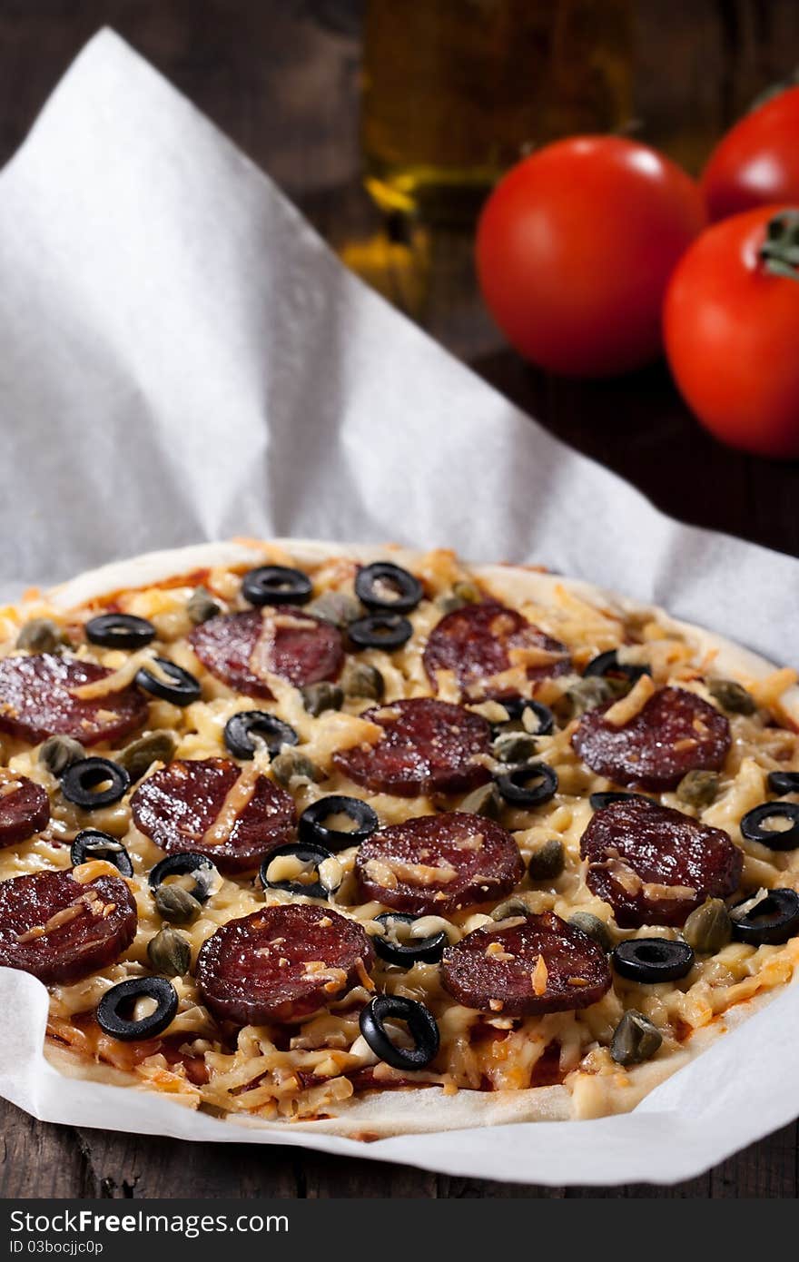 Homemade pizza with salami, cheese and black olives.