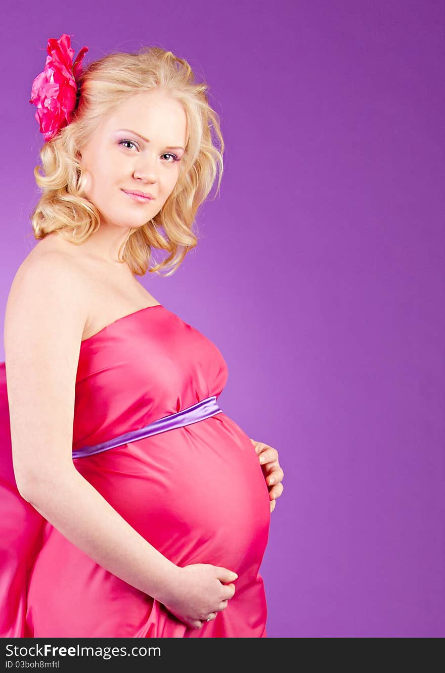 A young pregnant woman in a pink dress on the purple background. A young pregnant woman in a pink dress on the purple background