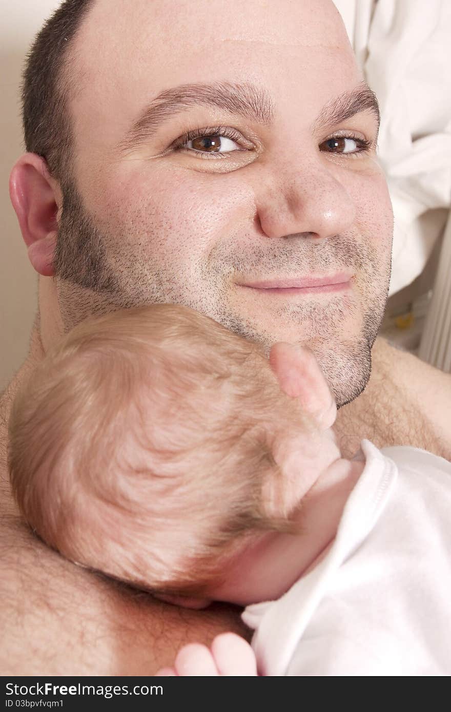 A father cuddles his newborn baby on his shoulder and looks at camera. A father cuddles his newborn baby on his shoulder and looks at camera