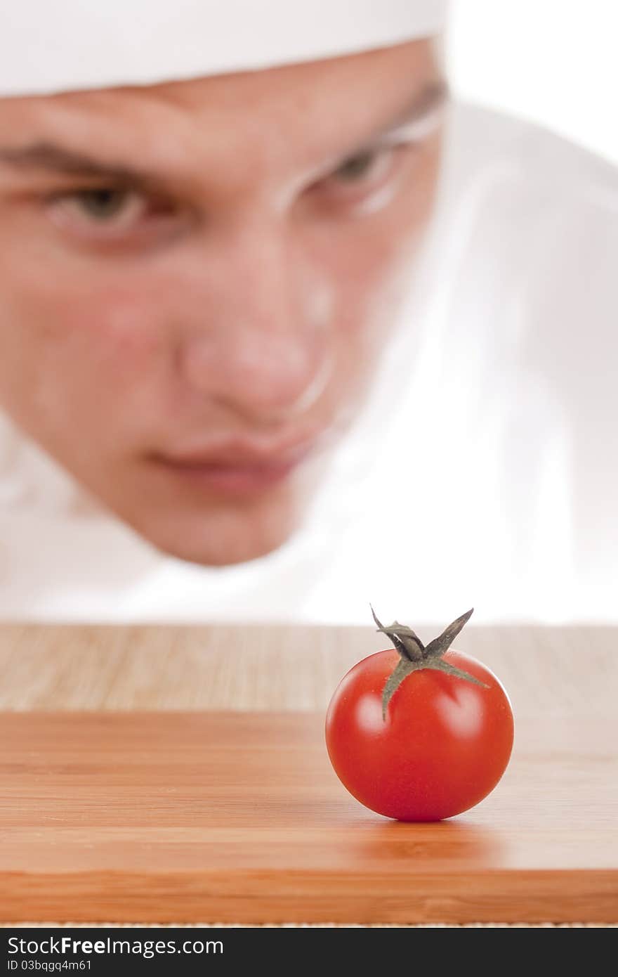 The young chef in chef's hat is considering a tomato. The young chef in chef's hat is considering a tomato.