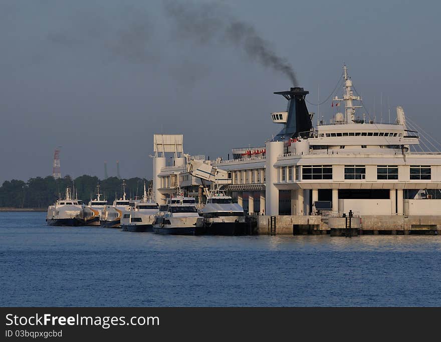 Ferry terminal with a big ship releasing black smoke from it's funnel.