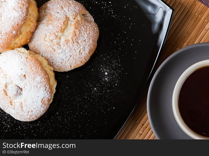 Muffins with a sugar powder on a black plate and a cup of tea