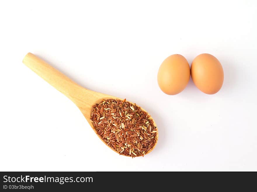 Brown egg and wooden spoon with red rice; on a white background