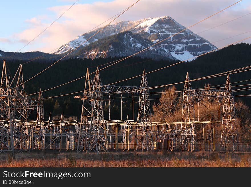 Electric power lines and power station from the Bonneville Dam on the Columbia River. Pink clouds in blue sky, snowy hillside. Electric power lines and power station from the Bonneville Dam on the Columbia River. Pink clouds in blue sky, snowy hillside.