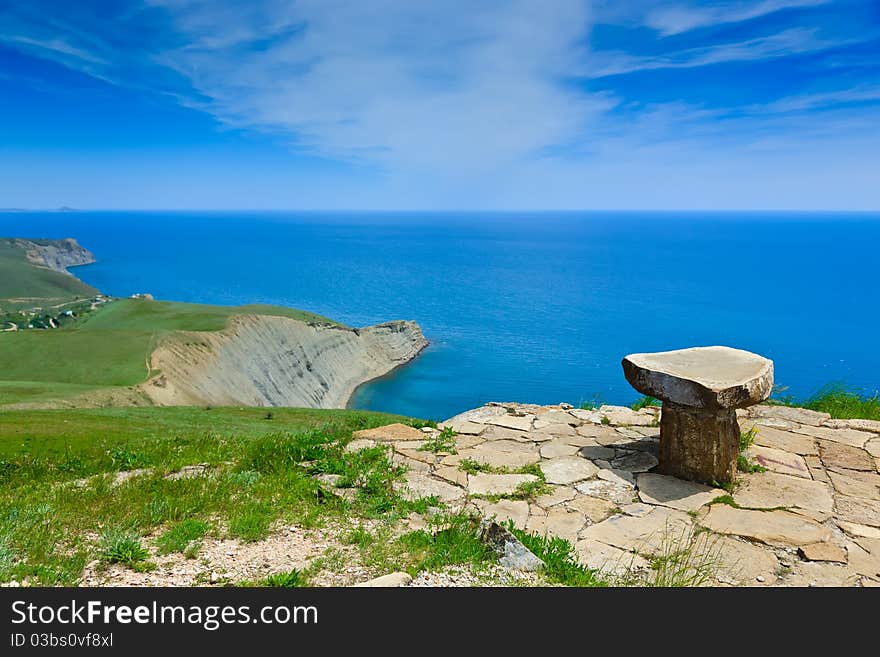 Stone seat on mountain above the sea on a background of the sky with clouds. Stone seat on mountain above the sea on a background of the sky with clouds