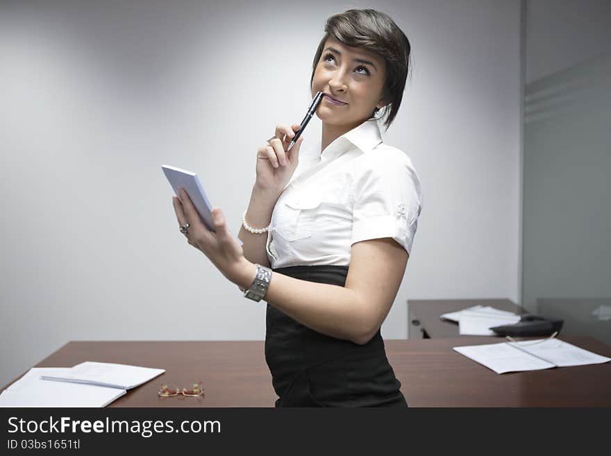 Smiling person dressed as businesswoman, thinking with a pen and a piece of paper on her hands. Smiling person dressed as businesswoman, thinking with a pen and a piece of paper on her hands