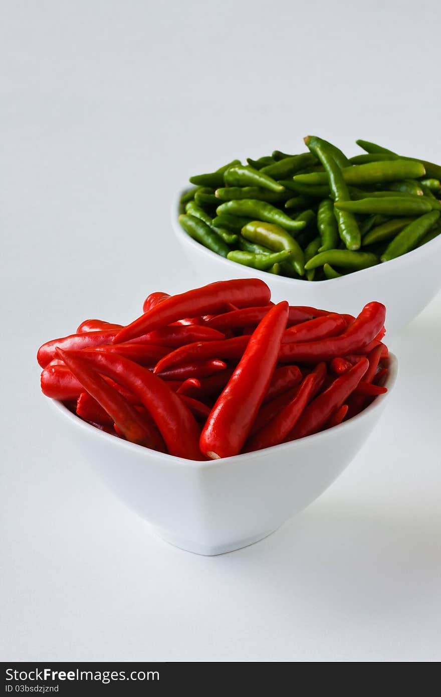 Red and green chili peppers in white cups on white background