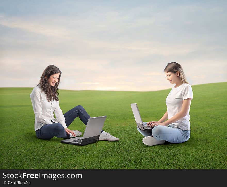 Beautiful women using laptops on a green meadow. Beautiful women using laptops on a green meadow