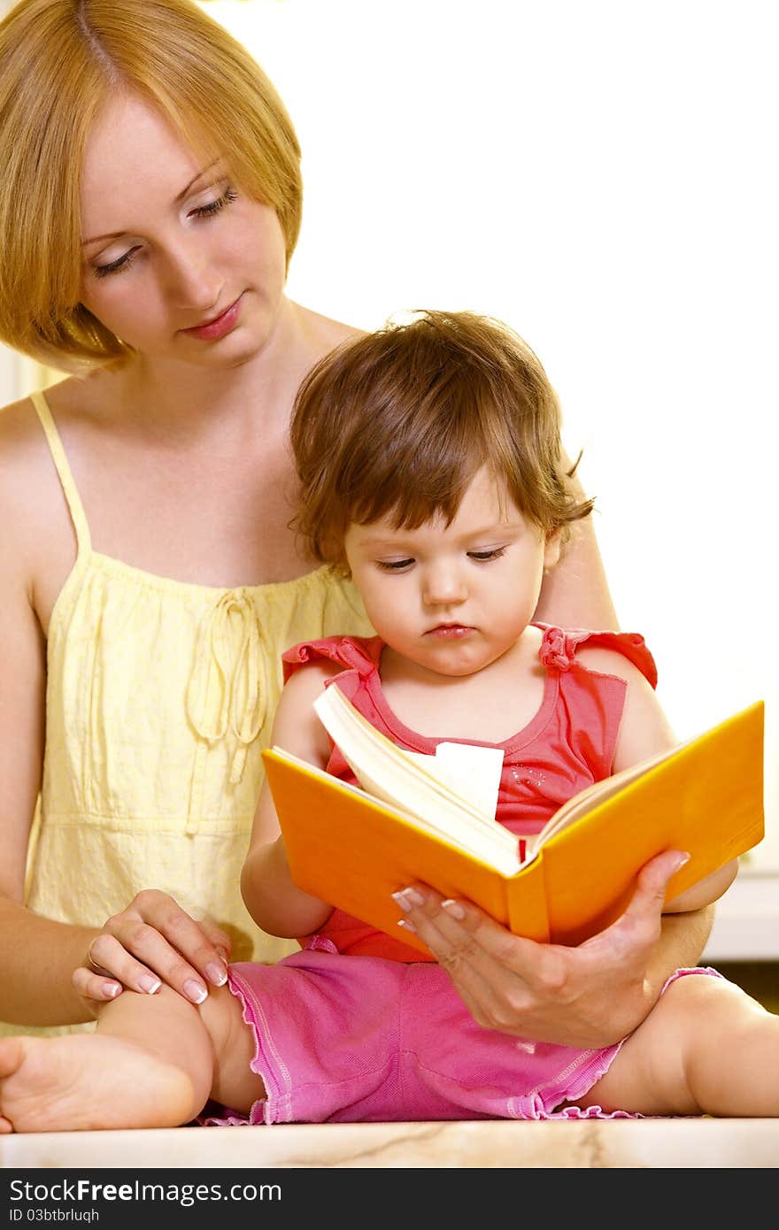 Young mother with her daughter reading book at home