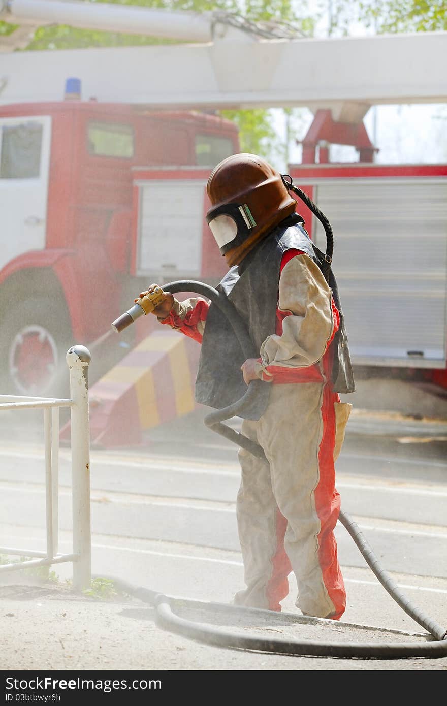 Worker in a protective suit spraying sand with abrasive peeler