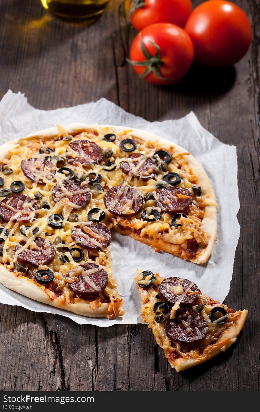 Homemade pizza with salami, cheese and black olives.