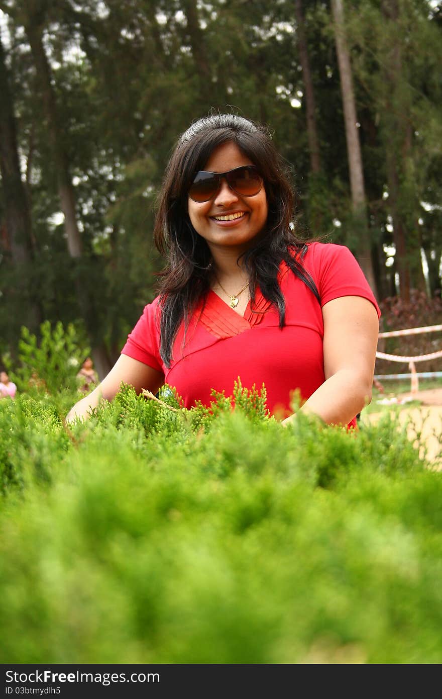 Good looking woman in red dress wearing shades behind waist height bushes. Good looking woman in red dress wearing shades behind waist height bushes.