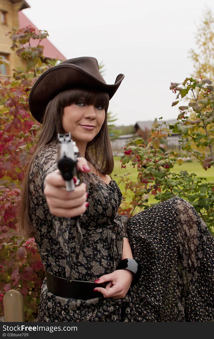 Young girl wearing long dress and leather hat points her gun toward the viewer. Young girl wearing long dress and leather hat points her gun toward the viewer