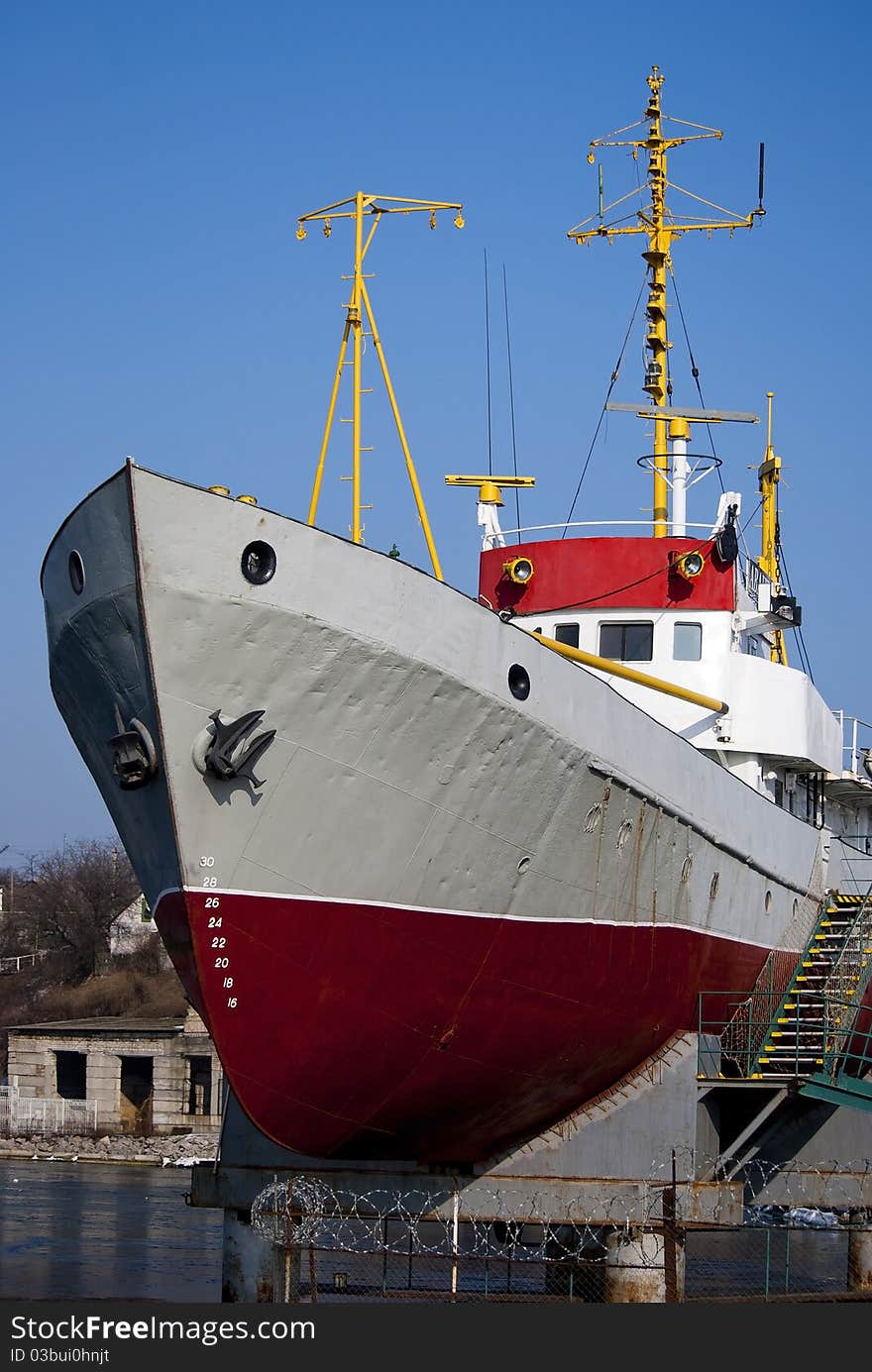 Ship with yellow masts and red bottom against blue sky