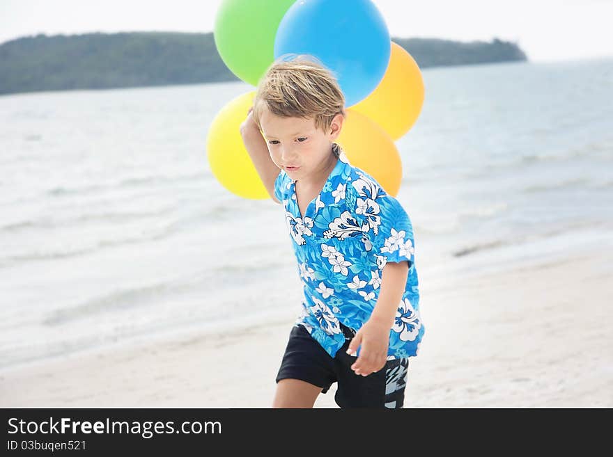 Young happy boy running with balloons on beach