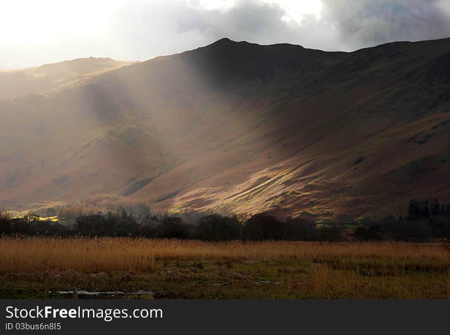 Sun breaks through the winter cloud and illuminates a dark fell. Lake District, Cumbria, England. Sun breaks through the winter cloud and illuminates a dark fell. Lake District, Cumbria, England.