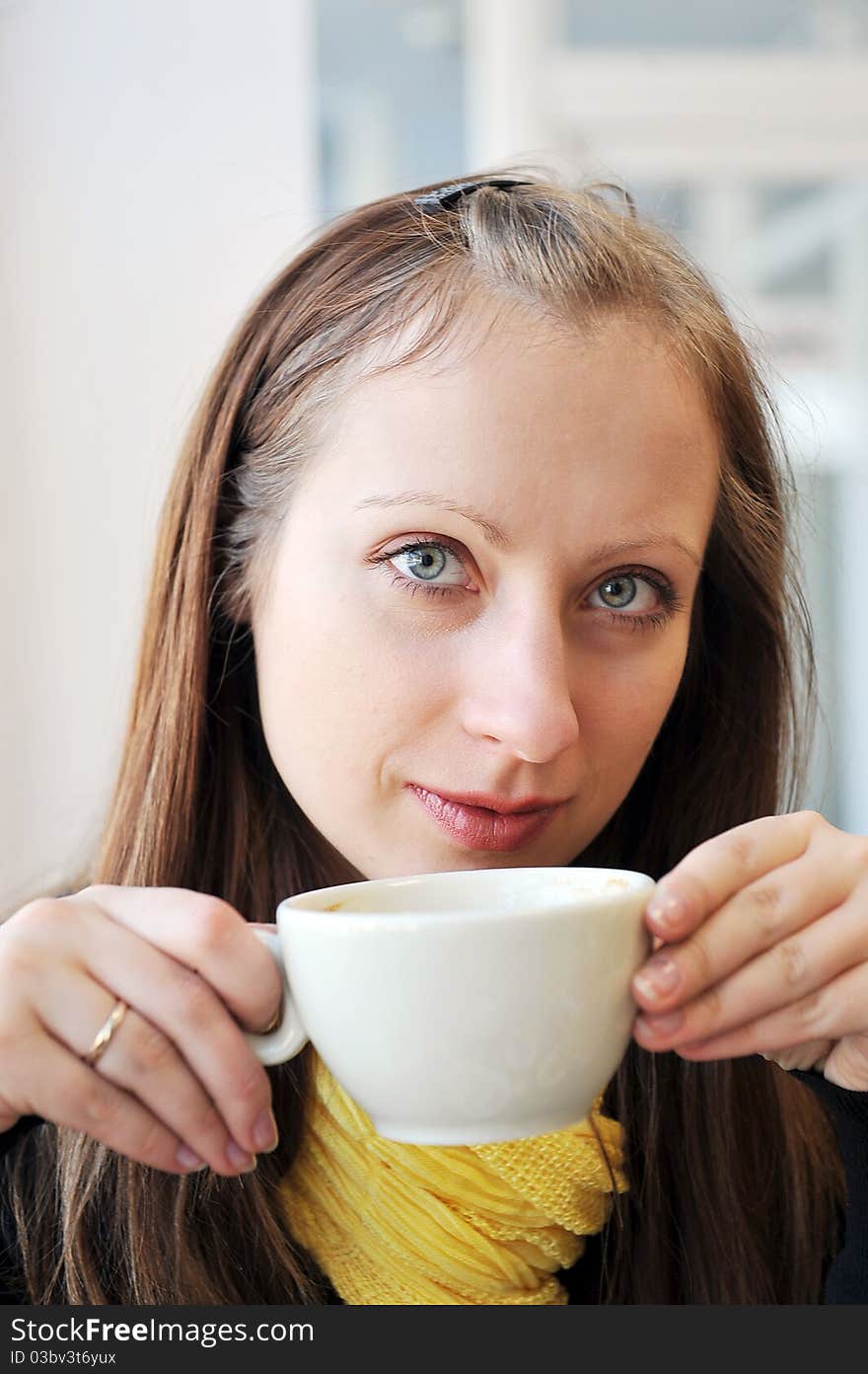 Young woman holding cup of coffee and looking out window. She drinks coffee at cafe