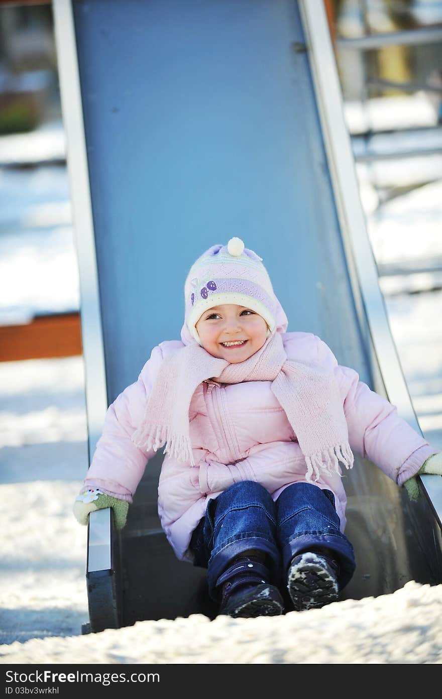 Small beautiful girl sits on  children's hill. Winter day