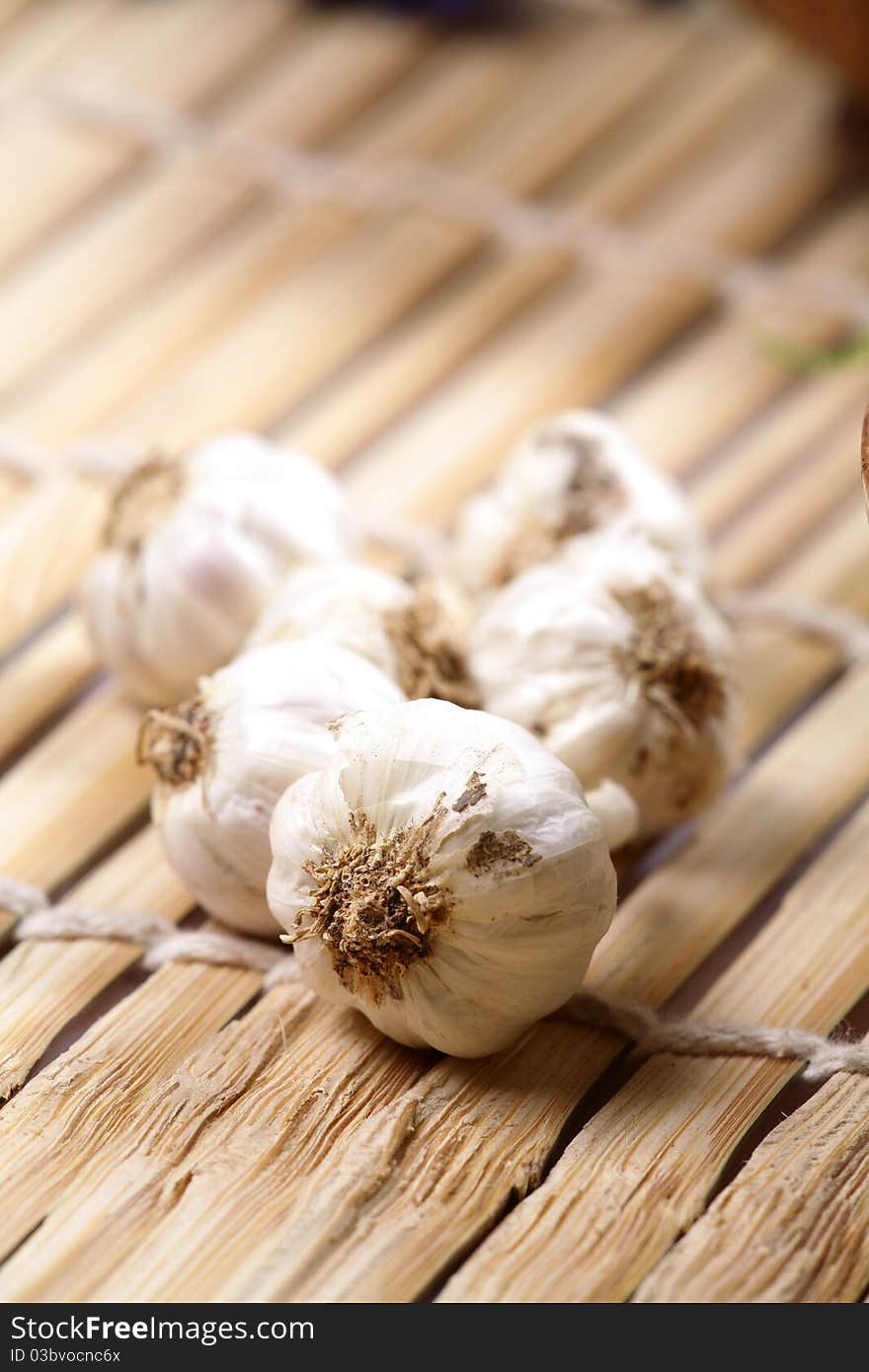 Closeup shot of white garlic pods over wooden mat.