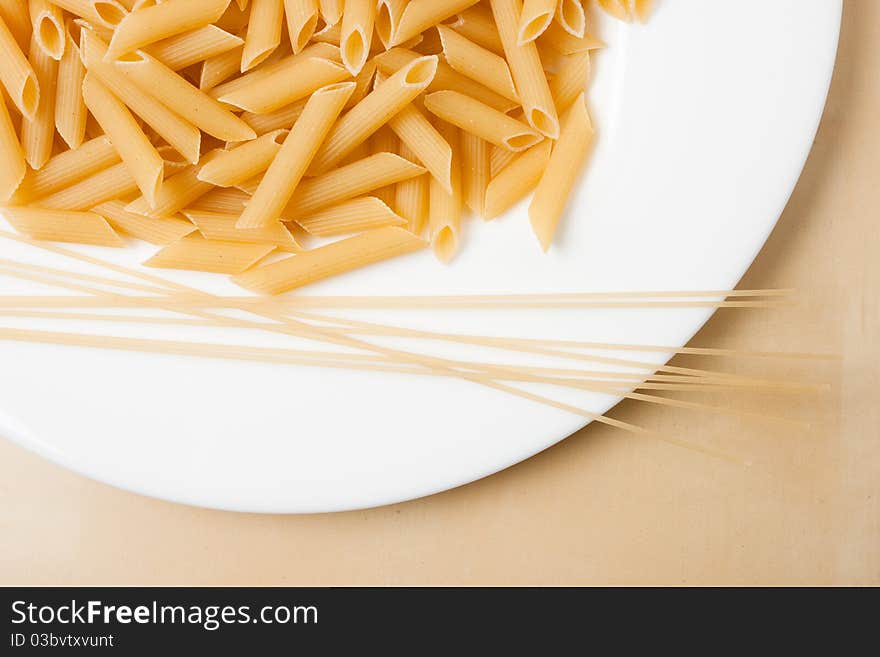 Raw pasta on white plate, on wooden table