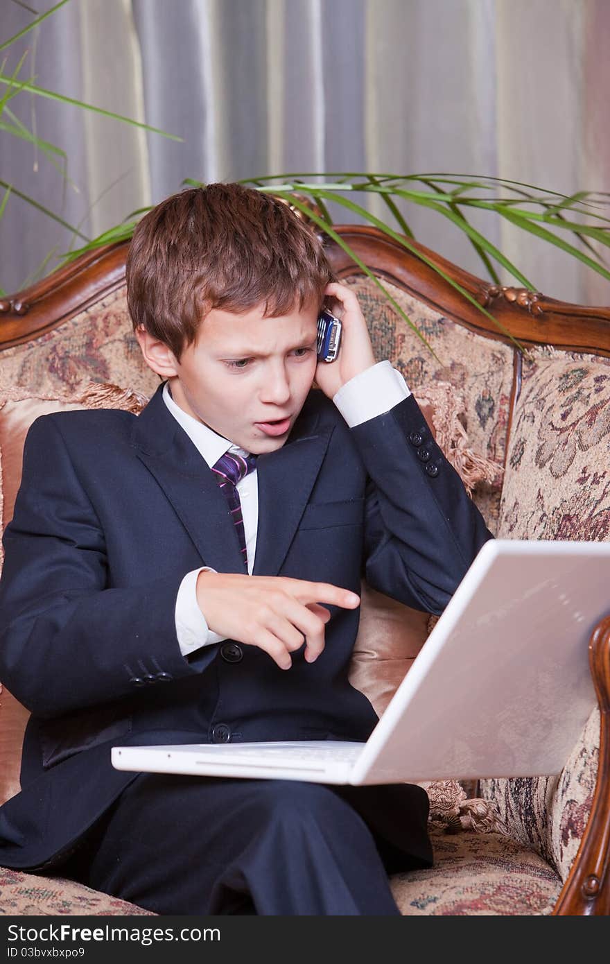 Young angry confident businessman talking on cell pointing at computer. Young angry confident businessman talking on cell pointing at computer