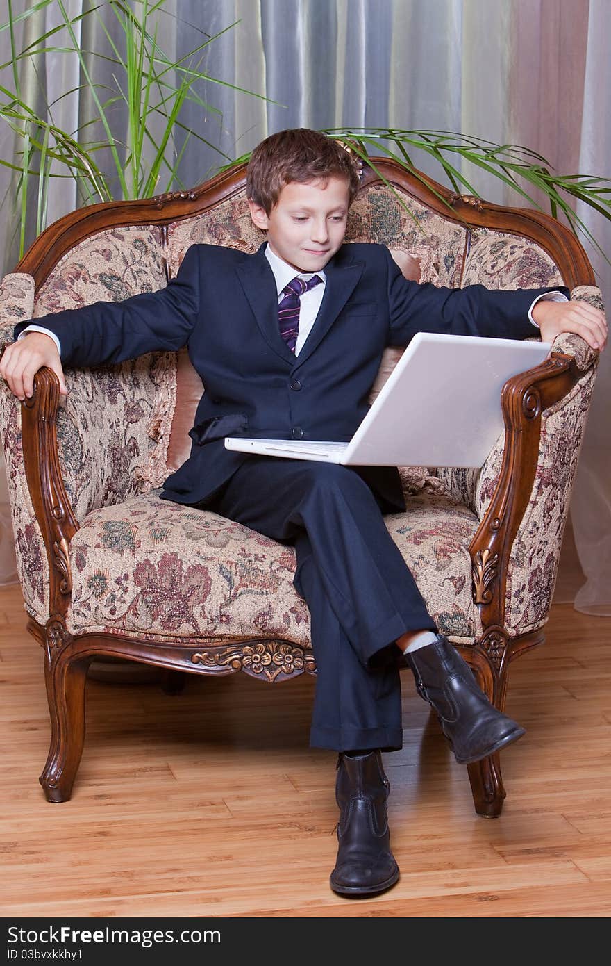 Young smiling boy dressed in business suite looking at white notebook. Young smiling boy dressed in business suite looking at white notebook