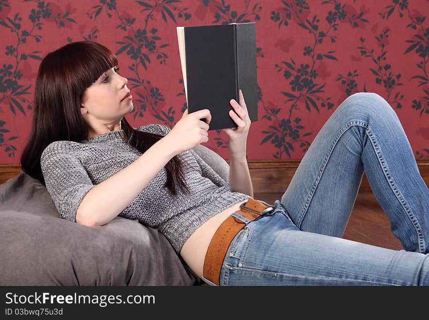 Pretty young woman lying on bean bag reading book