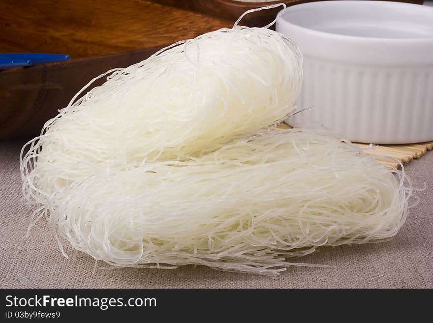 Close-up of raw white rice noodles on brown background.