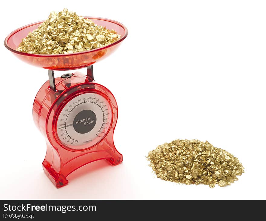 Red kitchen scales with a pile of gold being weighed and a pile of gold by the side of it