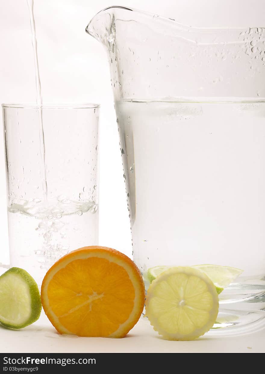 Slice of Lemon, Lime and Orange with a glass and jug. The glass has water being poured into it. Slice of Lemon, Lime and Orange with a glass and jug. The glass has water being poured into it.