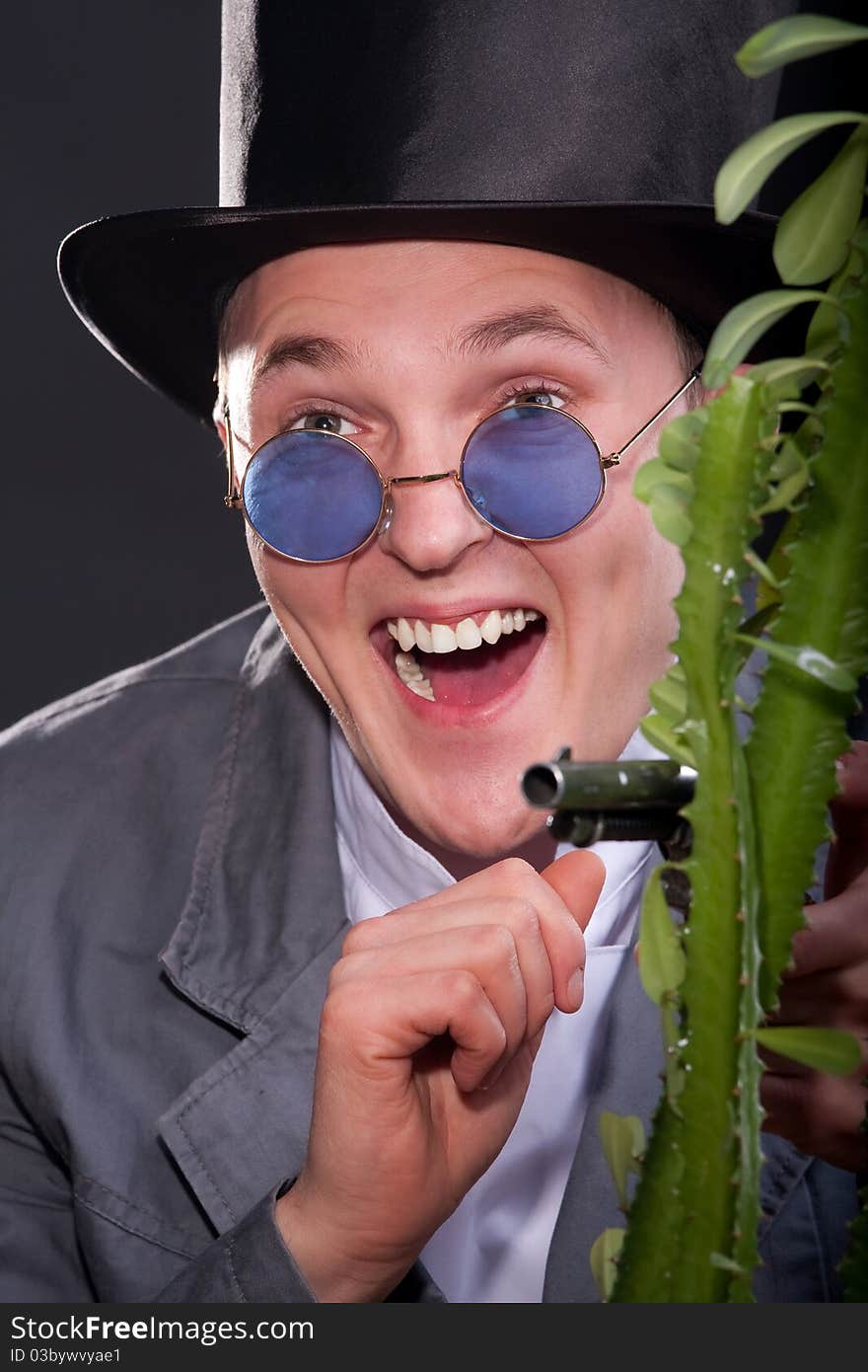 Emotional portrait of a man in a hat with a gun in his hand peek out from behind a plant