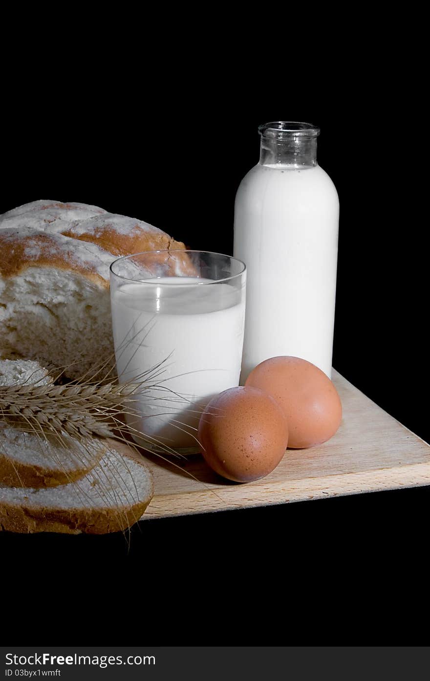 Bottle and cup of milk, eggs and bread on black