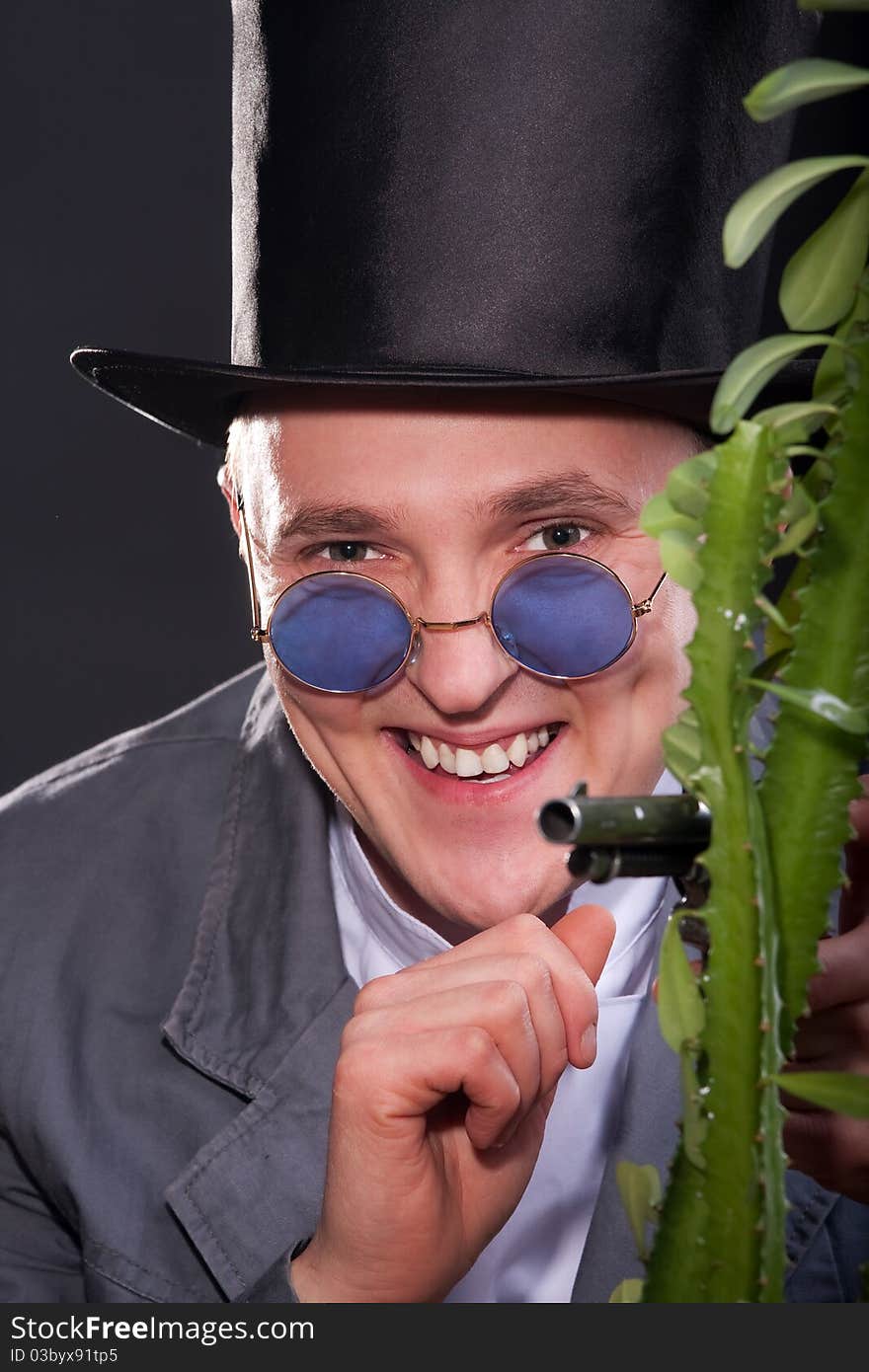 Emotional portrait of a man in a hat with a gun in his hand peek out from behind a plant