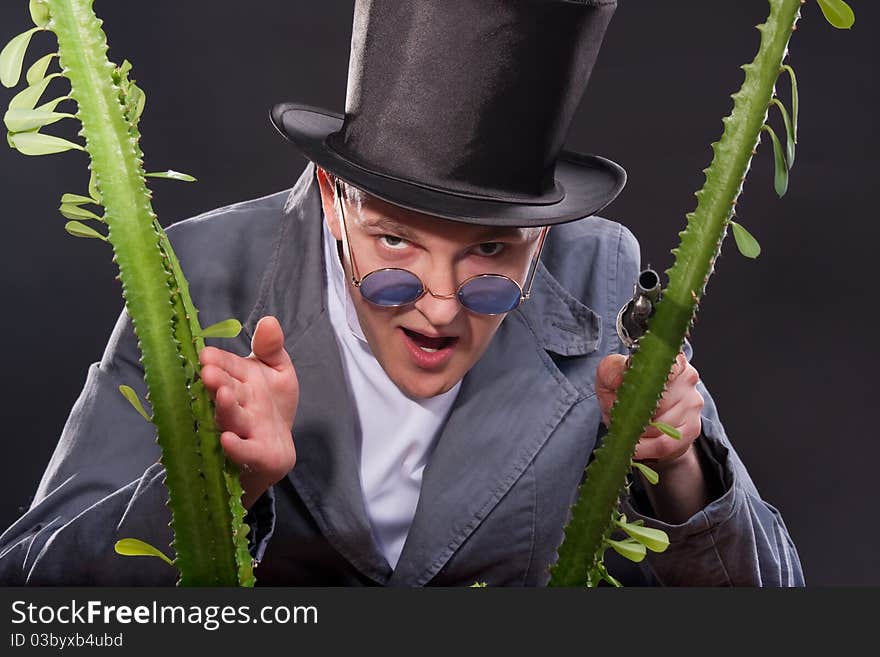 Emotional portrait of a man in a hat with a gun in his hand peek out from behind a plant