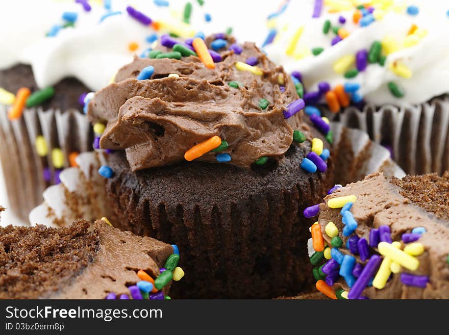 A macro image of chocolate cupcakes with festive sprinkles in sweet icing, wrap partially pulled back on one cupcake to display the delicious chocoate cake;. A macro image of chocolate cupcakes with festive sprinkles in sweet icing, wrap partially pulled back on one cupcake to display the delicious chocoate cake;