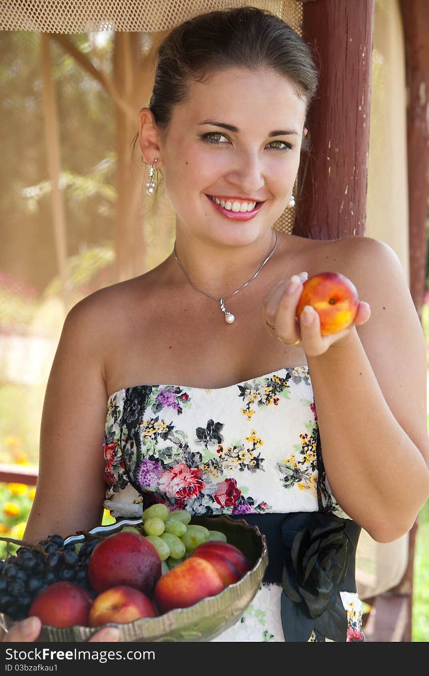 Beautiful brunette girl with fruits near the gazebo. Cheerful girl in a beautiful dress. Beautiful brunette girl with fruits near the gazebo. Cheerful girl in a beautiful dress.