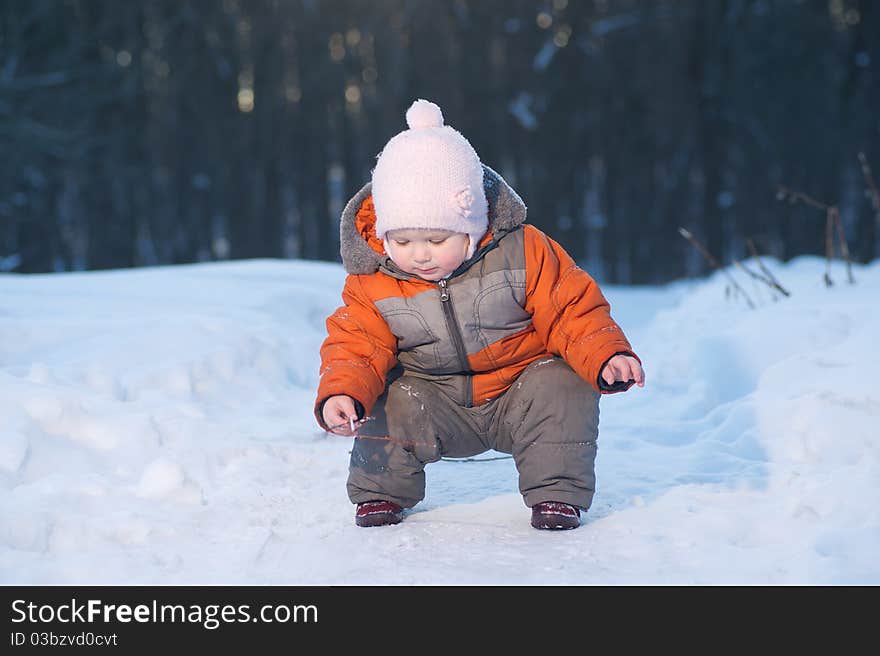 Adorable baby picking up small tree branch on snow road in park. Adorable baby picking up small tree branch on snow road in park