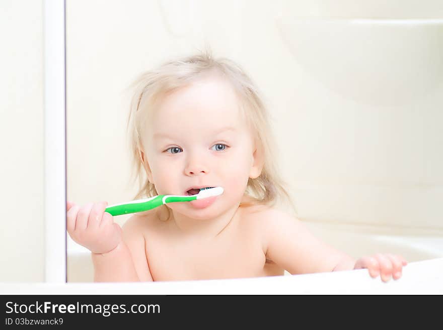 Adorable baby brushing teeth sitting in shower