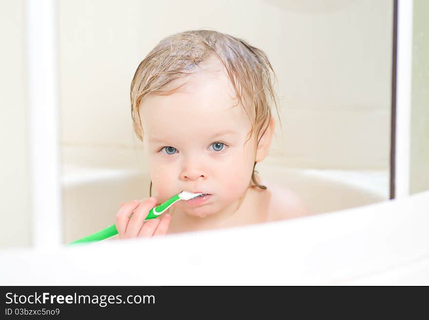 Adorable baby brushing teeth in shower