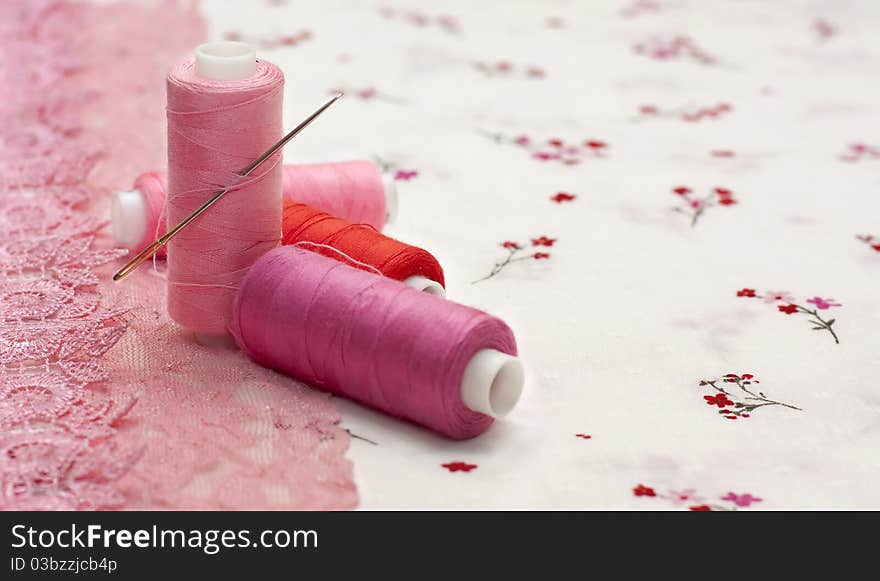 Pink spool of thread on a floral fabric background