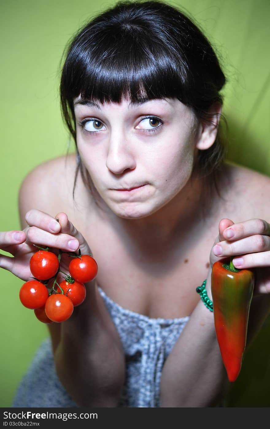 Girl holding tomato and pepper undecided. Girl holding tomato and pepper undecided