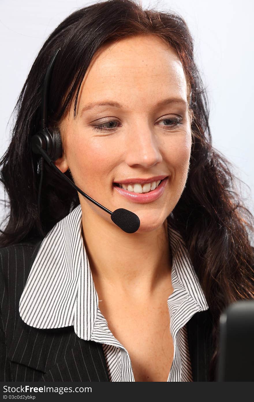 Beautiful young woman working in telesales with a smile, sitting to her computer speaking on a telephone headset. She is wearing a dark business suit. Beautiful young woman working in telesales with a smile, sitting to her computer speaking on a telephone headset. She is wearing a dark business suit.