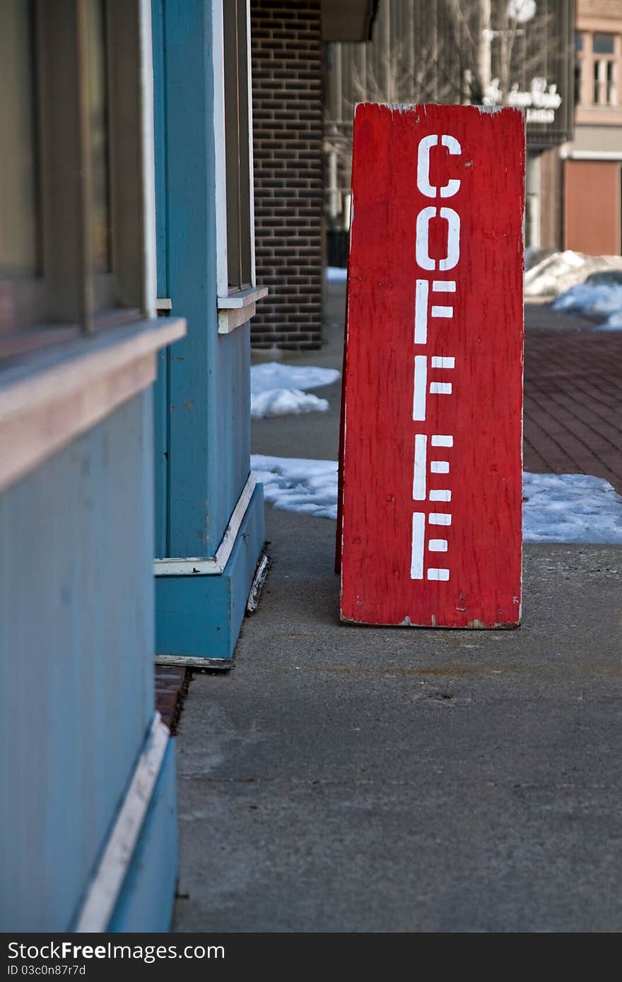 A red wooden sign sits on the sidewalk in front of a coffee shop. A red wooden sign sits on the sidewalk in front of a coffee shop